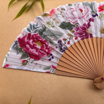 Floral-patterned hand fan with wooden frame and pink tassel on a beige background