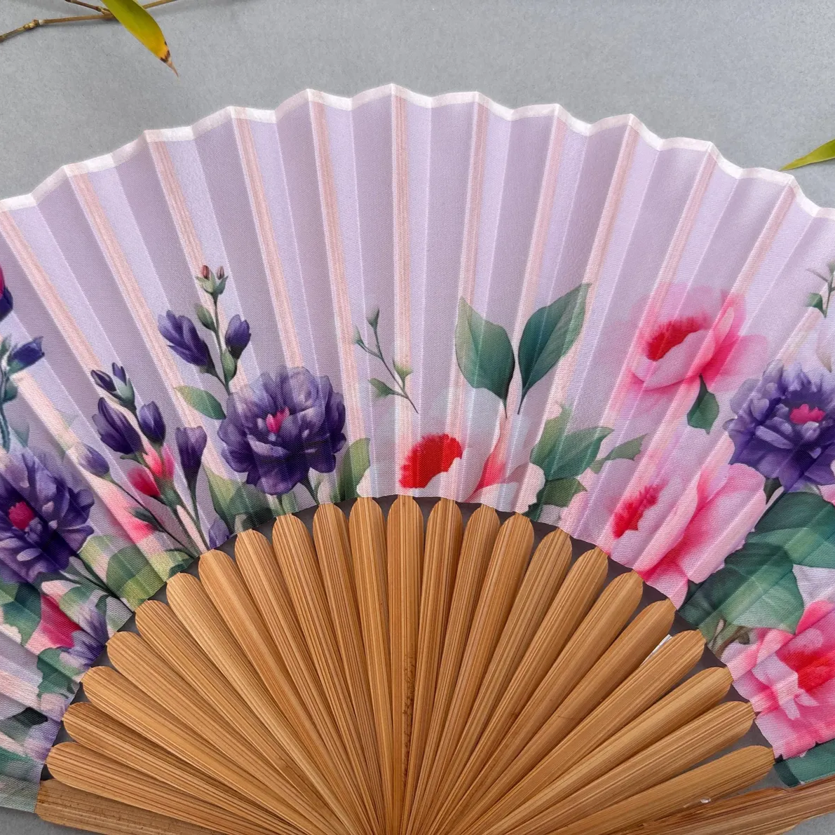 Handheld fan with floral design on a gray background
