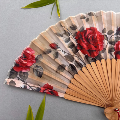 Handheld fan with red floral design on a gray background