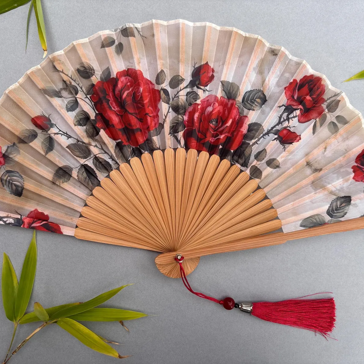 Handheld fan with red floral design on a gray background