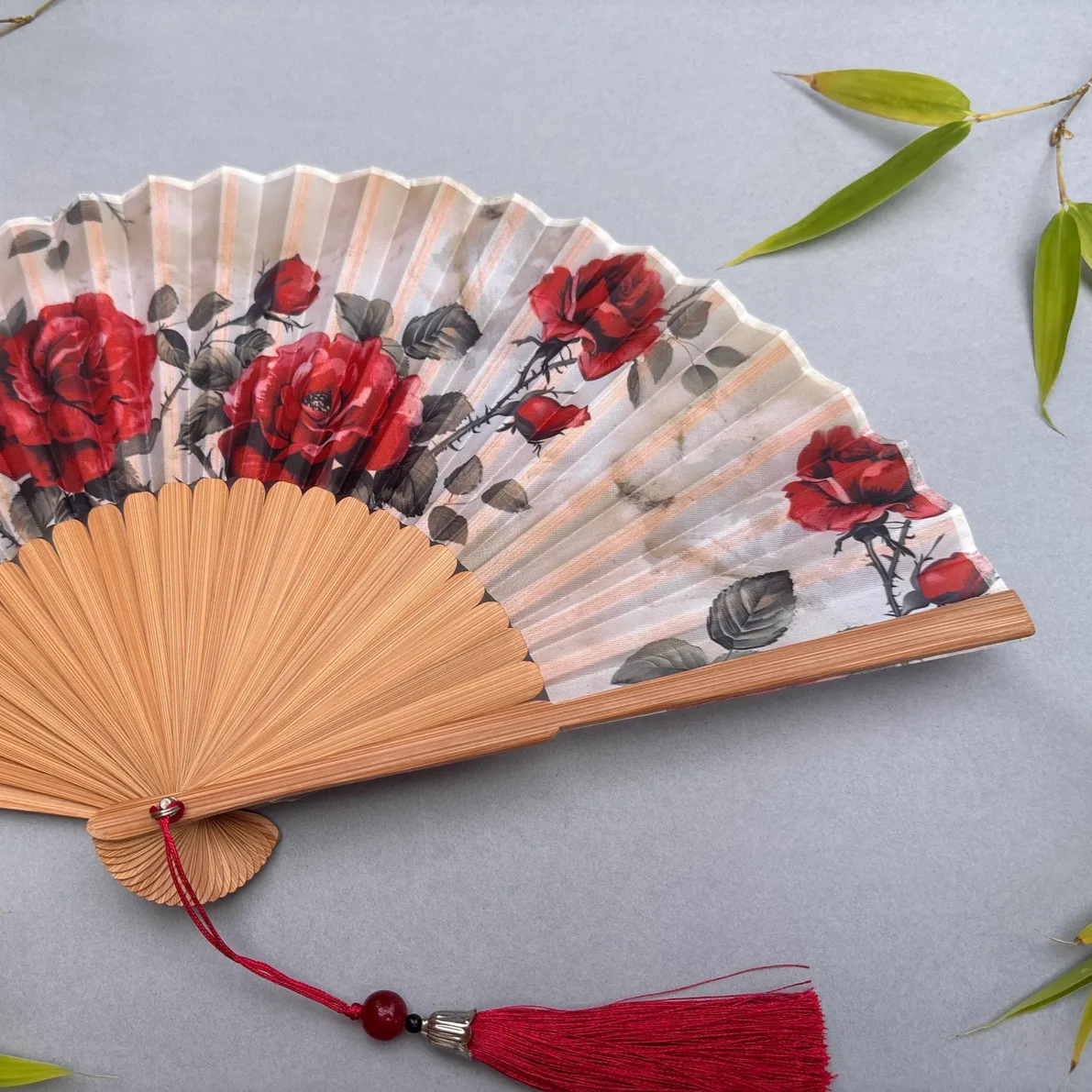 Handheld fan with red floral design on a gray background