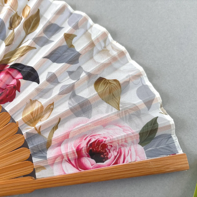 Floral-patterned hand fan with wooden frame and pink tassel on a gray background