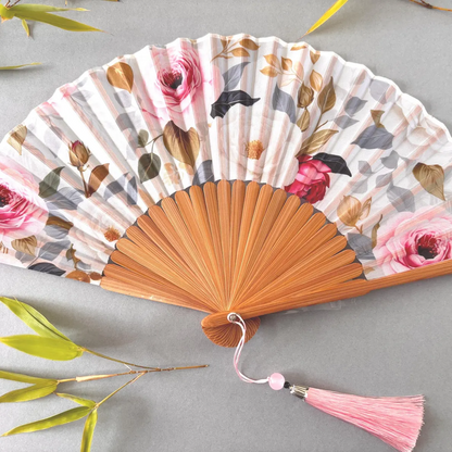 Floral-patterned hand fan with wooden frame and pink tassel on a gray background
