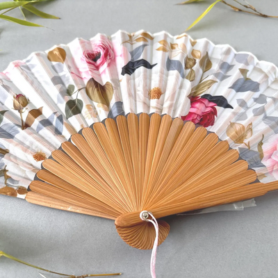 Floral-patterned hand fan with wooden frame and pink tassel on a gray background