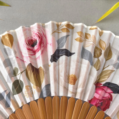 Floral-patterned hand fan with wooden frame and pink tassel on a gray background