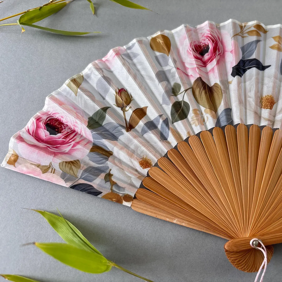 Floral-patterned hand fan with wooden frame and pink tassel on a gray background
