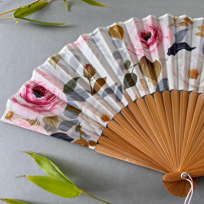 Floral-patterned hand fan with wooden frame and pink tassel on a gray background