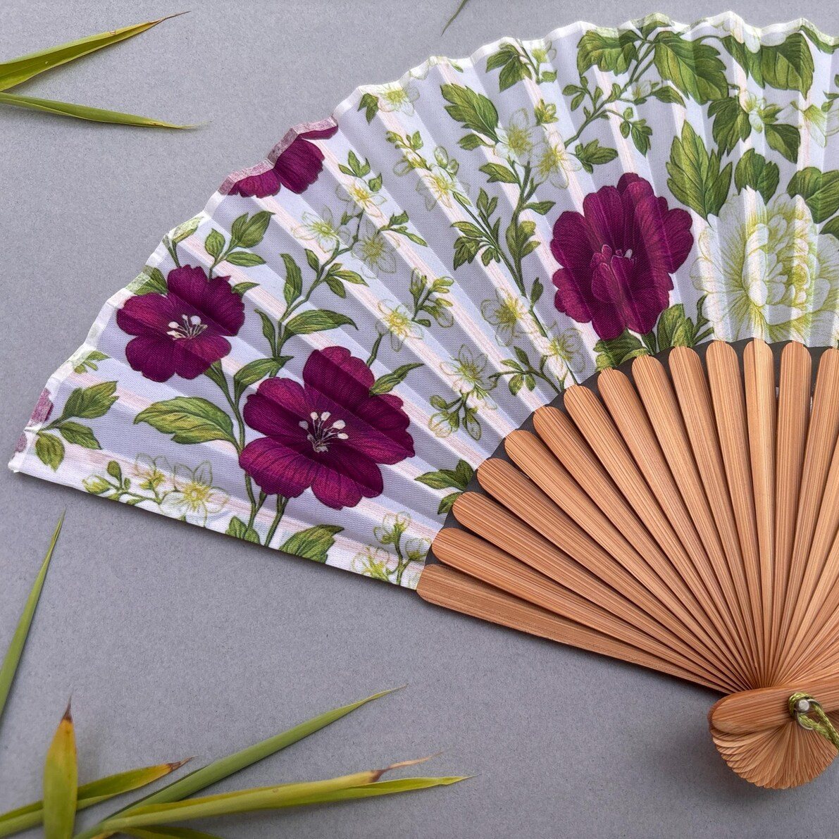 Floral-patterned hand fan with wooden handle on a gray background