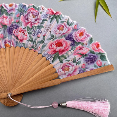 Floral-patterned hand fan with pink tassel on a gray background