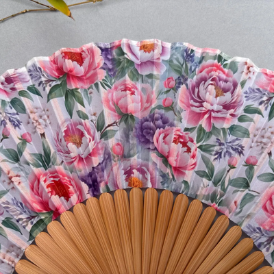 Floral-patterned hand fan with pink tassel on a gray background