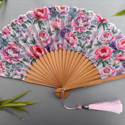 Floral-patterned hand fan with pink tassel on a gray background