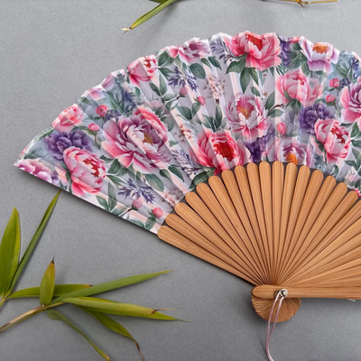 Floral-patterned hand fan with pink tassel on a gray background