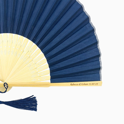 A folding fan with Navy Blue and beige hues features a stylish tassel. Its engraved text on the wooden rib, radiating elegance and charm.