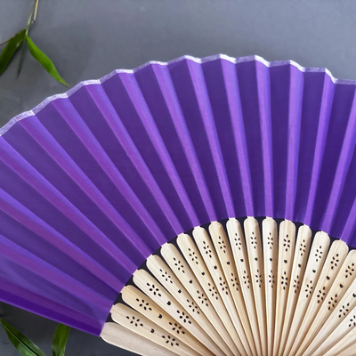 Purple hand fan with wooden handle on a dark background