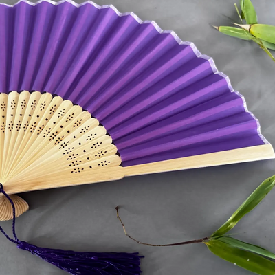 Purple hand fan with wooden handle on a gray background