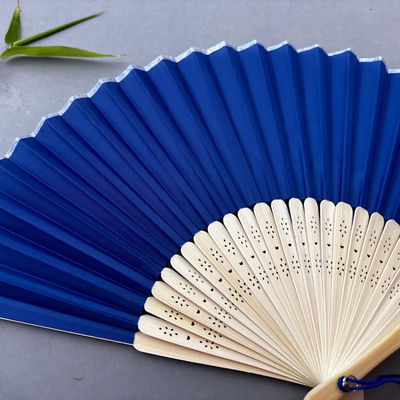 Blue folding fan with wooden handle on a gray background