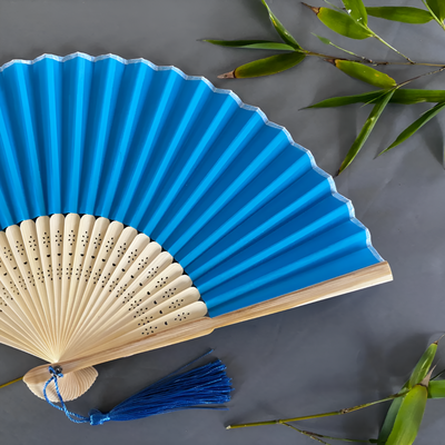 Blue and beige hand fan with tassel on a gray background with bamboo leaves