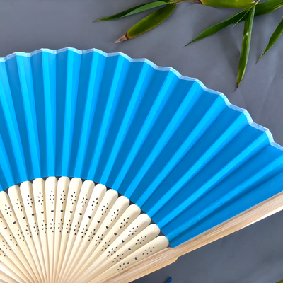 Blue hand fan with wooden handle on a gray background