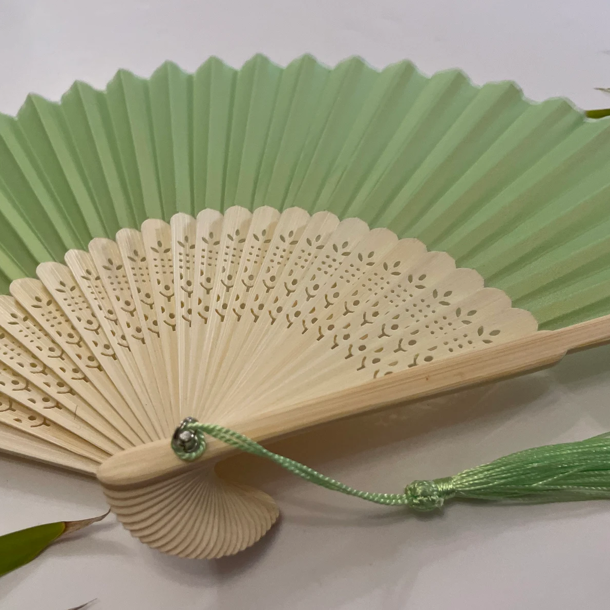 A mint green paper folding fan featuring a tassel, elegantly designed in a solid color.